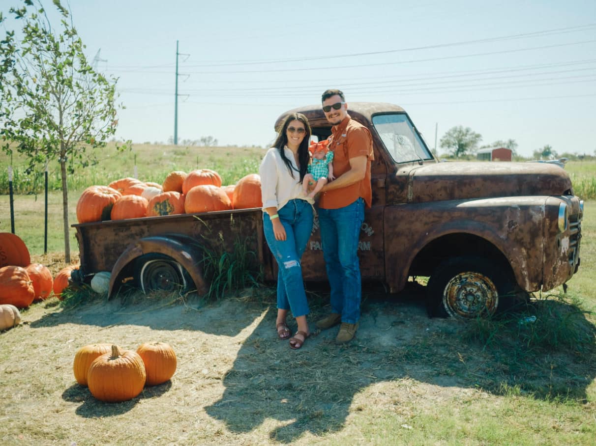 Realtor Elizabeth with her fiance and baby in front of truck filled with pumpkins